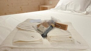 Ein ordentlich bezogenes Bett mit gefalteten Handtüchern, einer Flasche und einer kleinen Karte auf einer weißen Bettdecke in einem Zimmer mit Holzwänden.