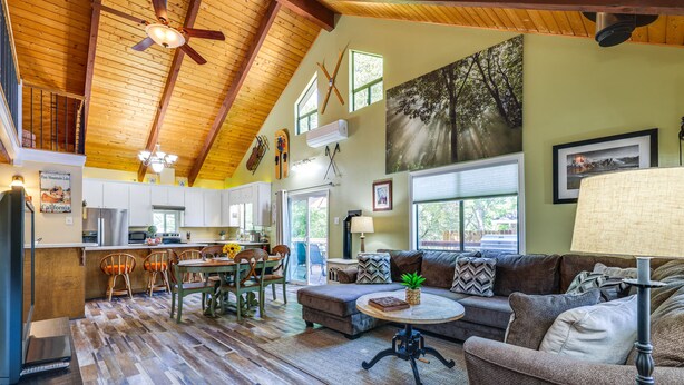 A spacious living area with a high ceiling, wooden flooring, a sofa, a coffee table, and a dining area with chairs and a table. - Groveland Home - Walk to Pine Mountain Lake! (Groveland)