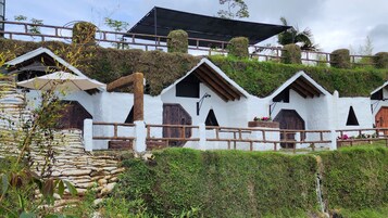 A row of white, thatched-roof cottages with wooden balconies, surrounded by greenery and a stone wall.