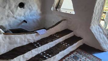 Interior rústico de pedra com uma pequena janela, um banco de madeira e um tapete estampado.