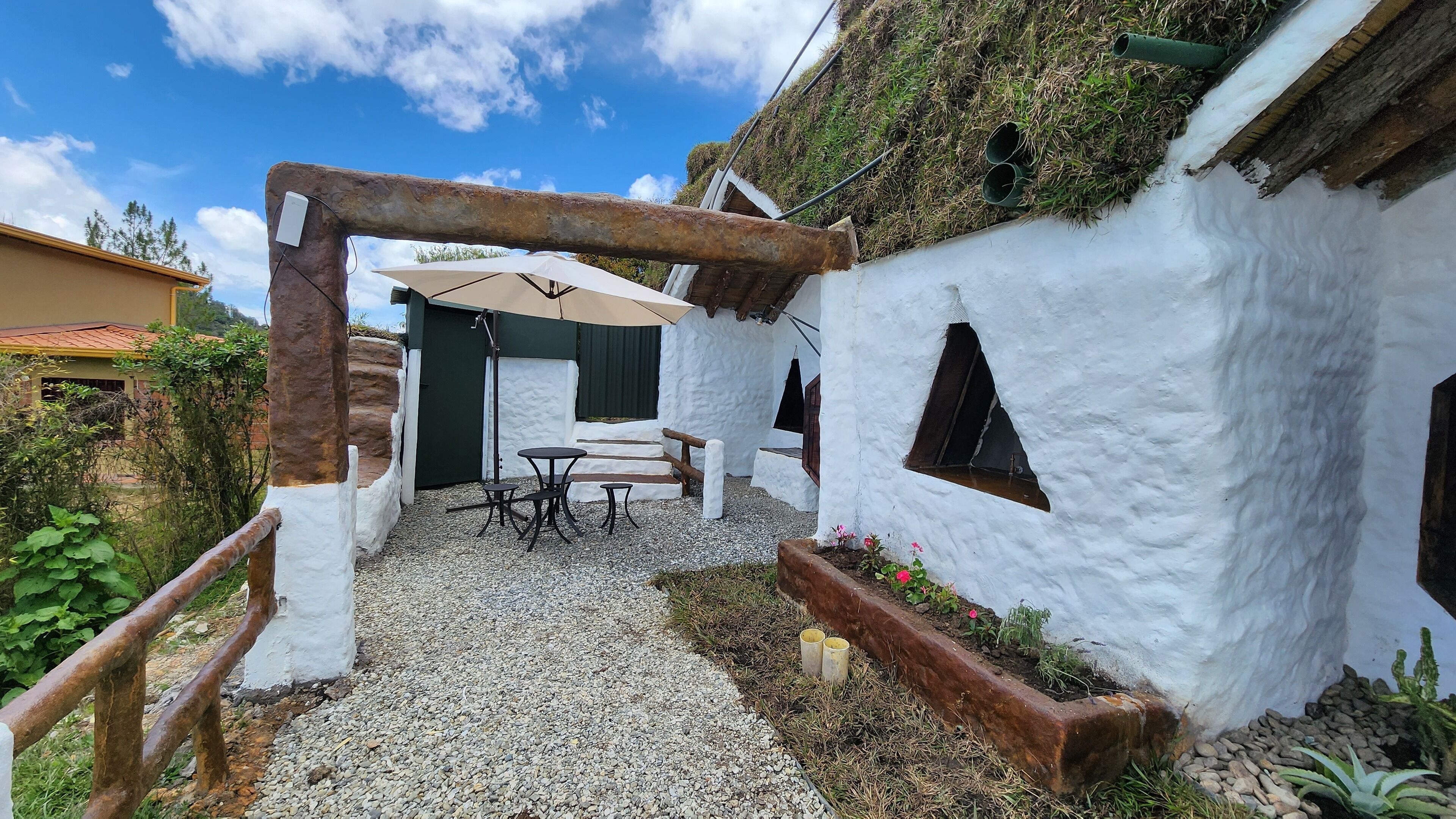 A rustic outdoor seating area with a table and chairs, surrounded by white walls and gravel ground.