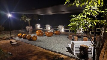 An outdoor seating area with round tables and chairs, surrounded by decorative planters and a palm tree.