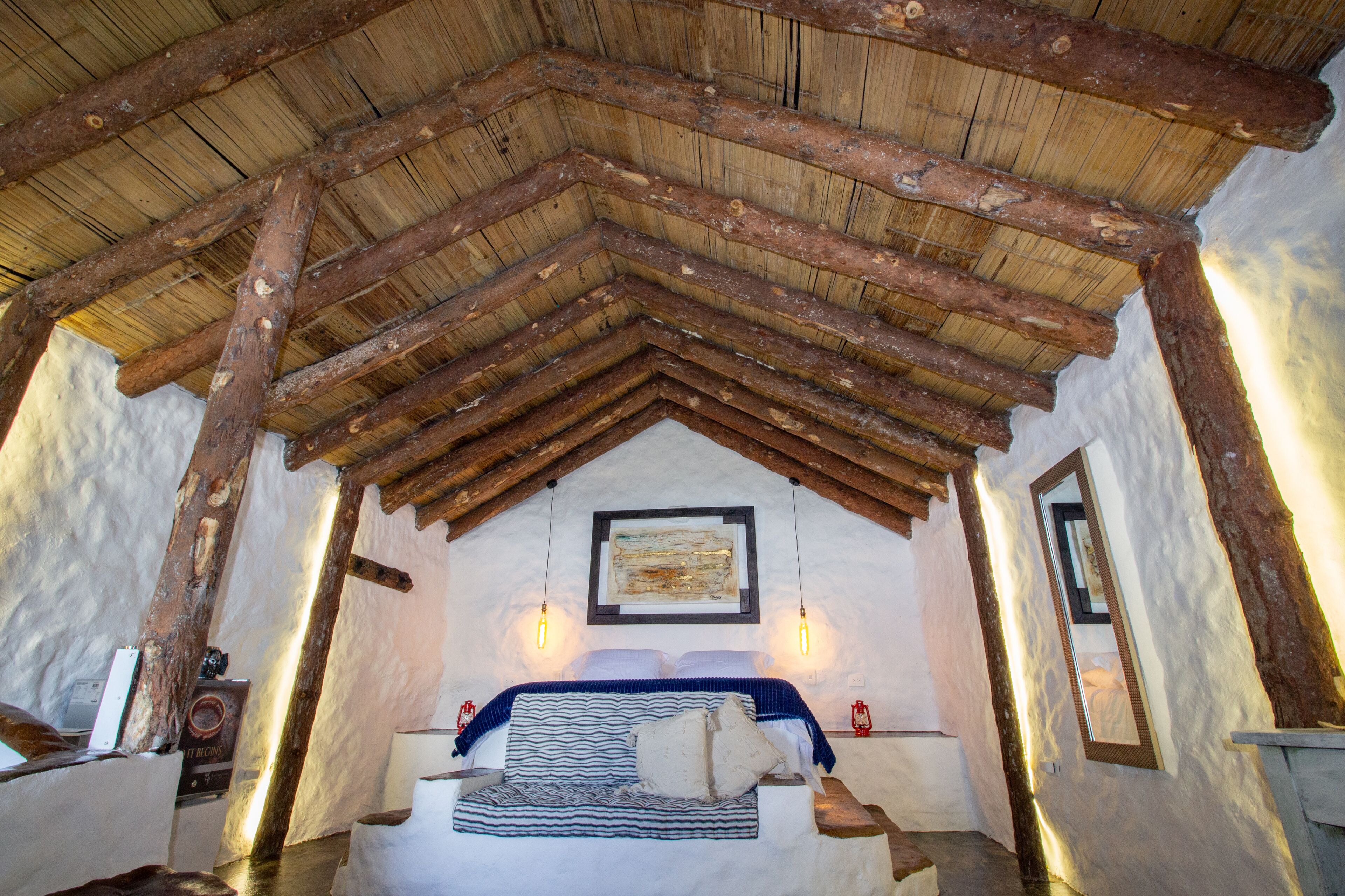Un dormitorio rústico con techo de madera, una cama con ropa de cama a rayas y dos lámparas fijadas a la pared.