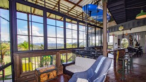 Una habitación amplia con grandes ventanales que ofrecen vistas al exterior, un banco de madera y una mesa con sillas.