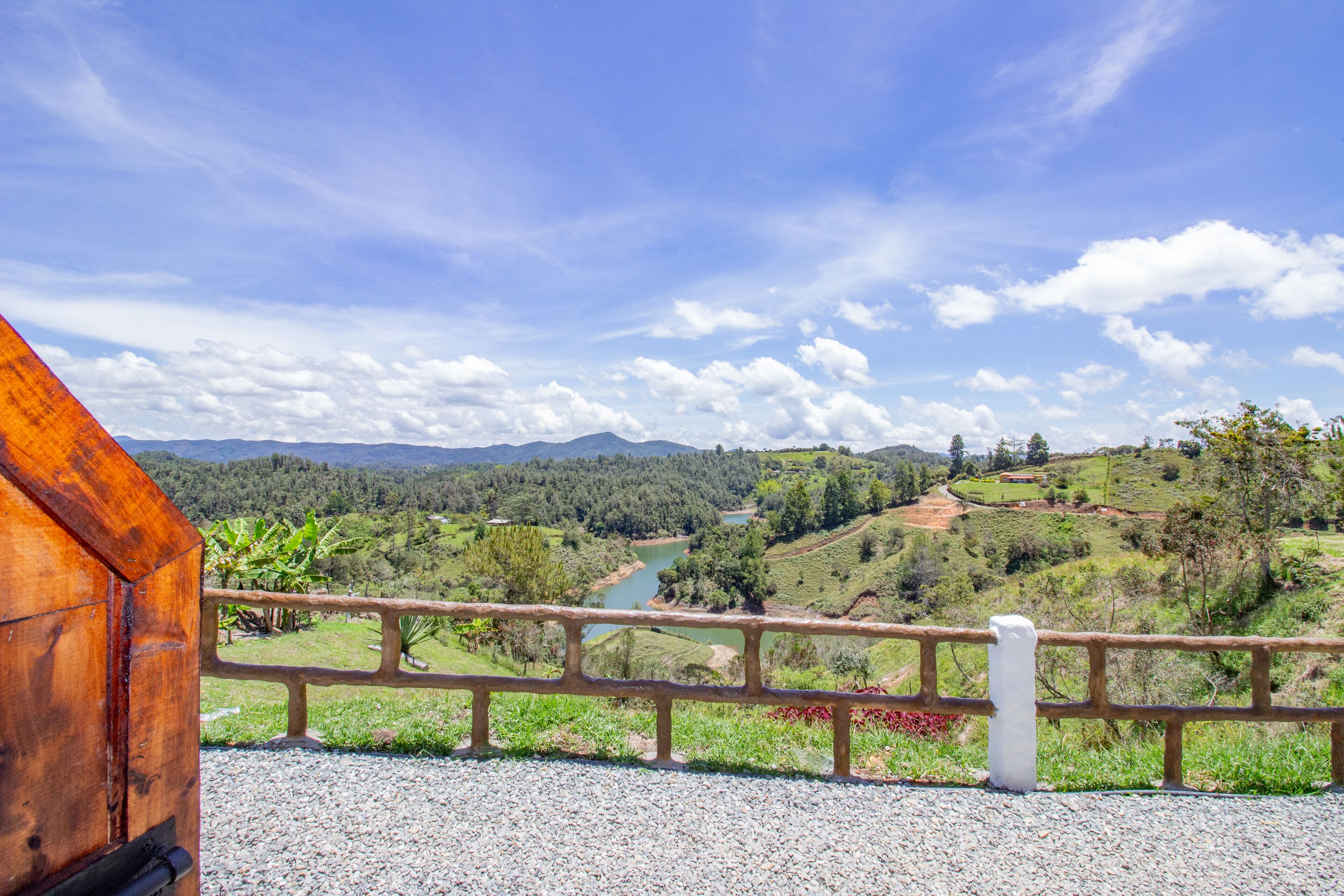 A scenic view from a wooden balcony overlooking a river, hills, and a clear sky.