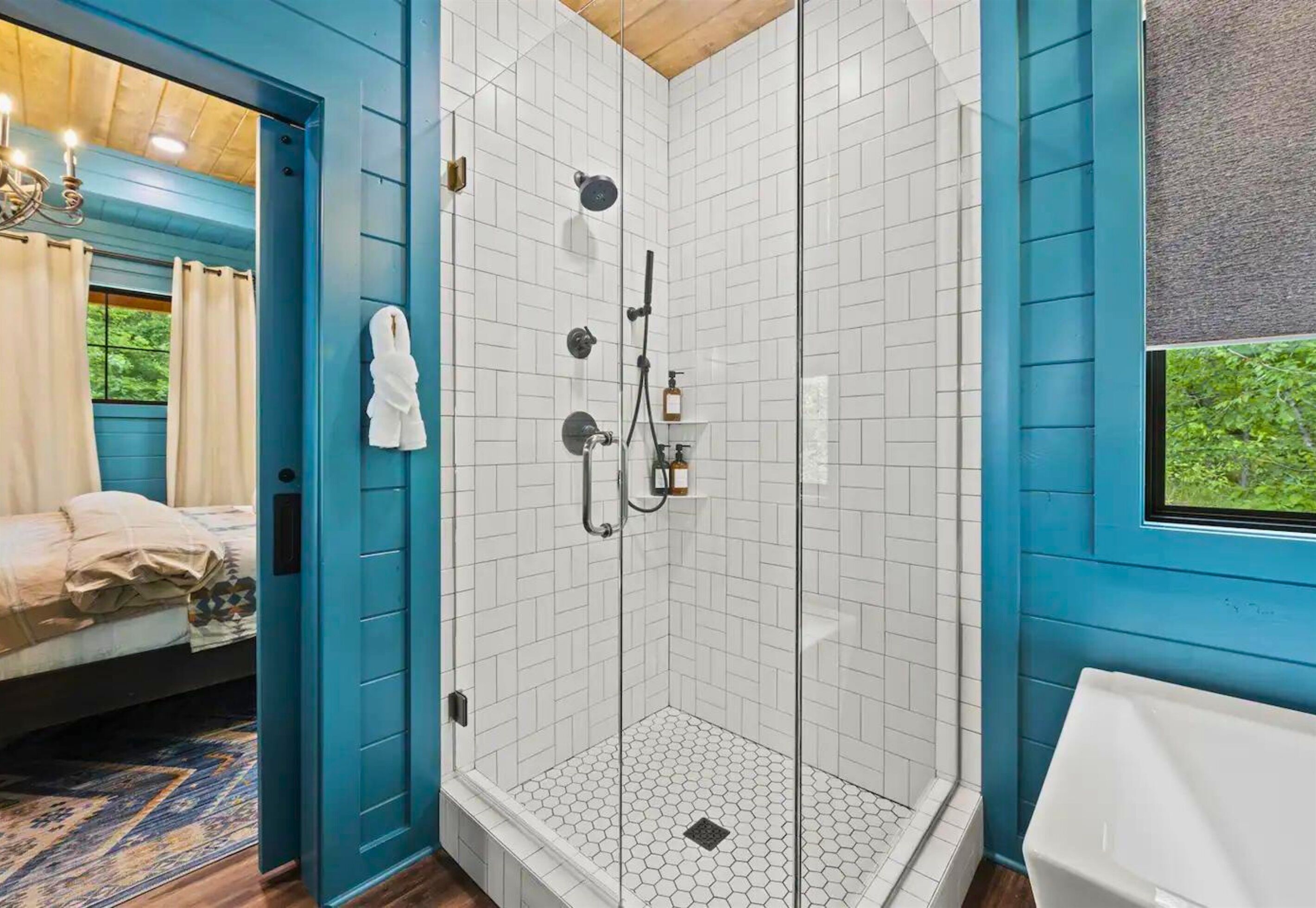 Une chambre dotée d’une douche en verre, d’un lit recouvert d’une courtepointe beige et d’une fenêtre donnant sur un paysage verdoyant.
