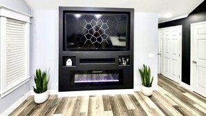 Una sala moderna con un mueble de entretenimiento negro, una chimenea y dos plantas en macetas.