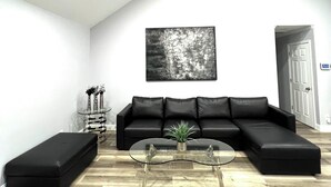 Una sala moderna con un sofá seccional de cuero negro, una mesa de centro de vidrio y un reposapiés negro. Hay una mesita auxiliar con una planta y un jarrón decorativo. Un cuadro abstracto negro adorna la pared sobre el sofá.