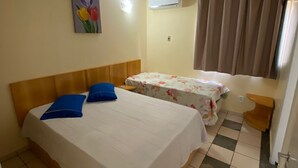 Une chambre d’hôtel avec deux lits, un tableau représentant des fleurs, un appareil de climatisation et un sol à carreaux.