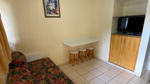 Une chambre à coucher avec un lit, un bureau avec des tabourets, une télévision et un tableau encadré au mur.