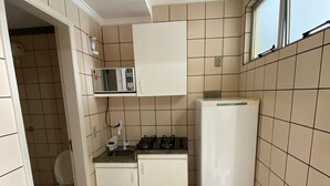 Une cuisine compacte avec des meubles blancs, un four à micro-ondes, une cuisinière à gaz et un réfrigérateur.