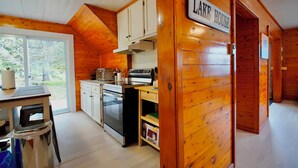 A cabin interior with wooden walls, a kitchen with white cabinets, a stove, and a dining area with a table and chairs.
