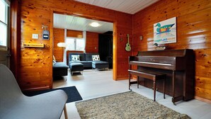 A wooden interior with a piano, a sofa, and a dining table.