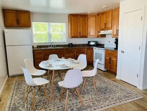 Una cocina con armarios de madera, un refrigerador, una estufa y una mesa de comedor con sillas blancas.