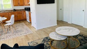 Una cucina moderna con mobili in legno, un forno a microonde e un'area pranzo con sedie bianche e un tappeto decorato.