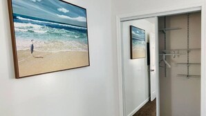 Una stanza con un quadro grande raffigurante una spiaggia, una porta scorrevole in vetro che dà su un armadio con ripiani, e un pavimento con tappeto.
