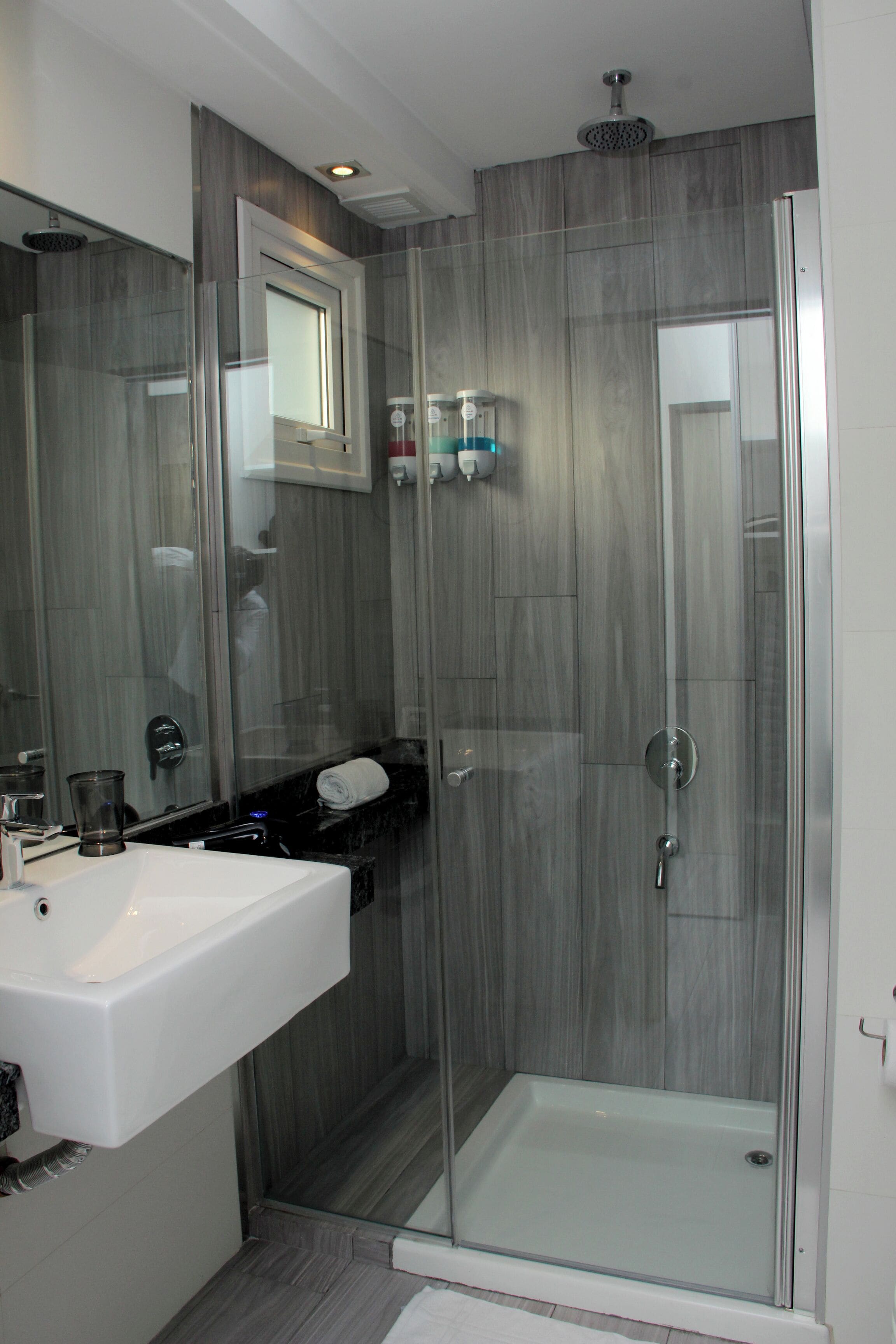 A modern bathroom with a glass-enclosed shower, a white sink, and a mirror above it.
