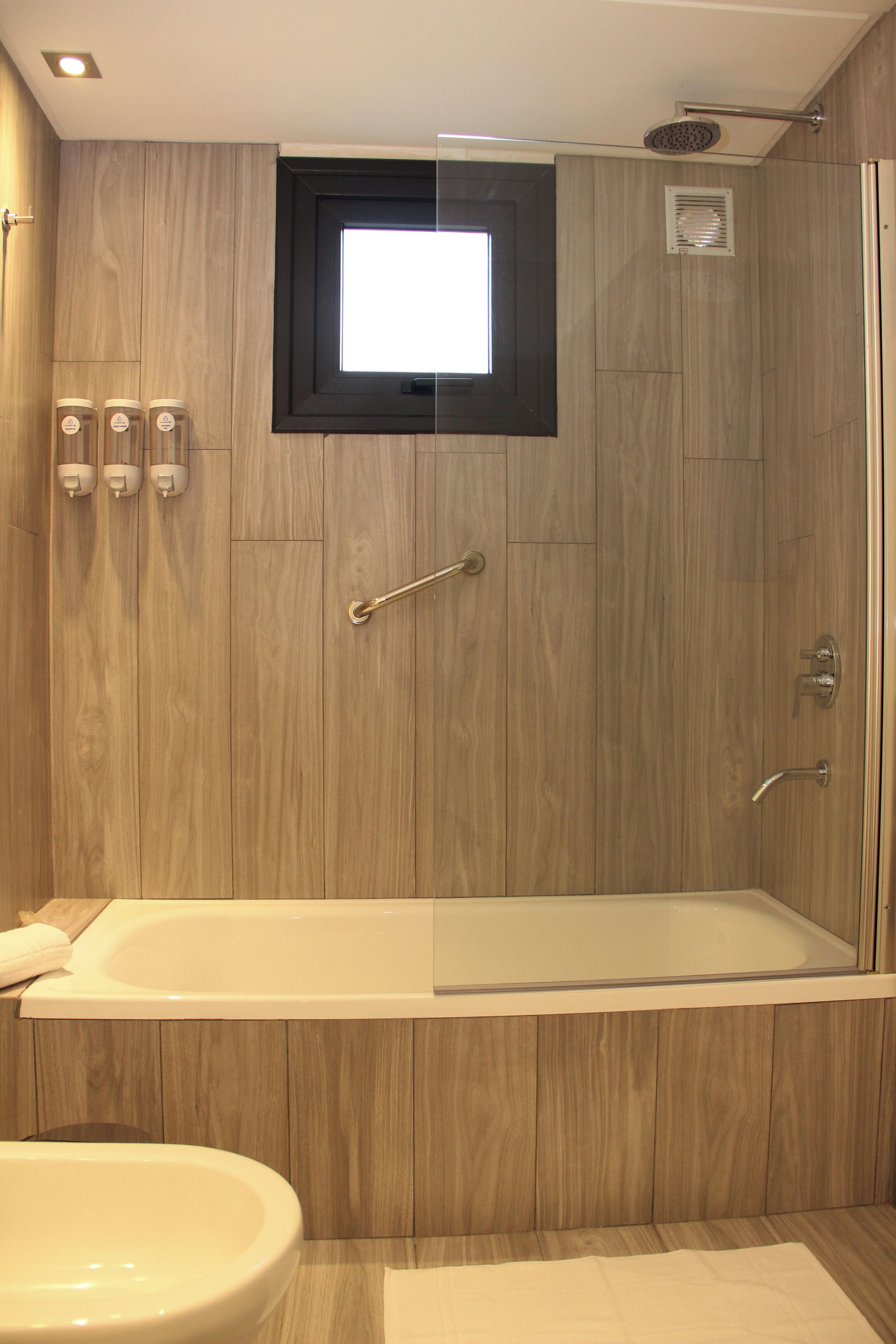 A modern bathroom with a wooden panel design, a glass-enclosed shower, and a bathtub.