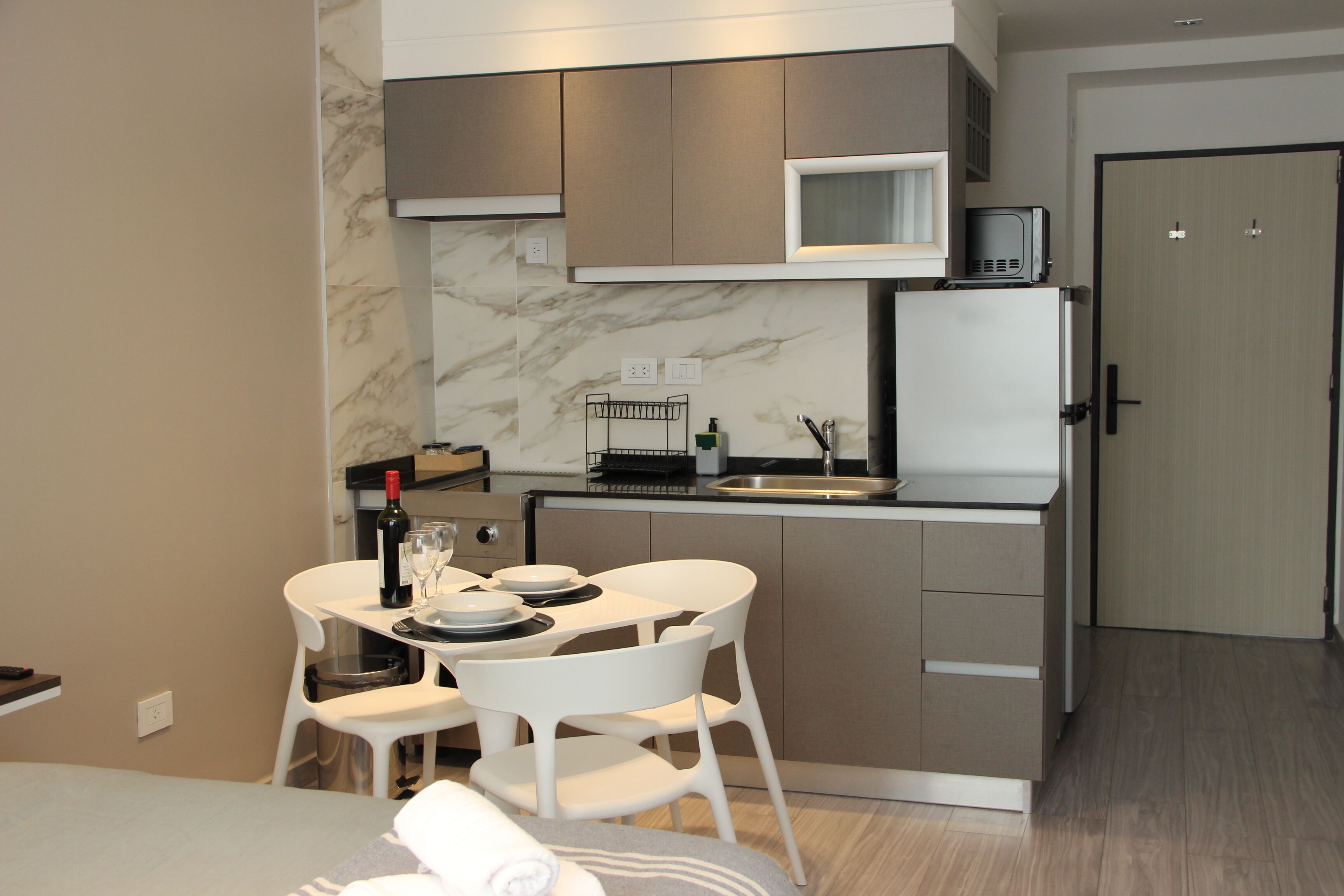 A compact kitchen with a microwave, refrigerator, and dining area with white chairs and a small table.