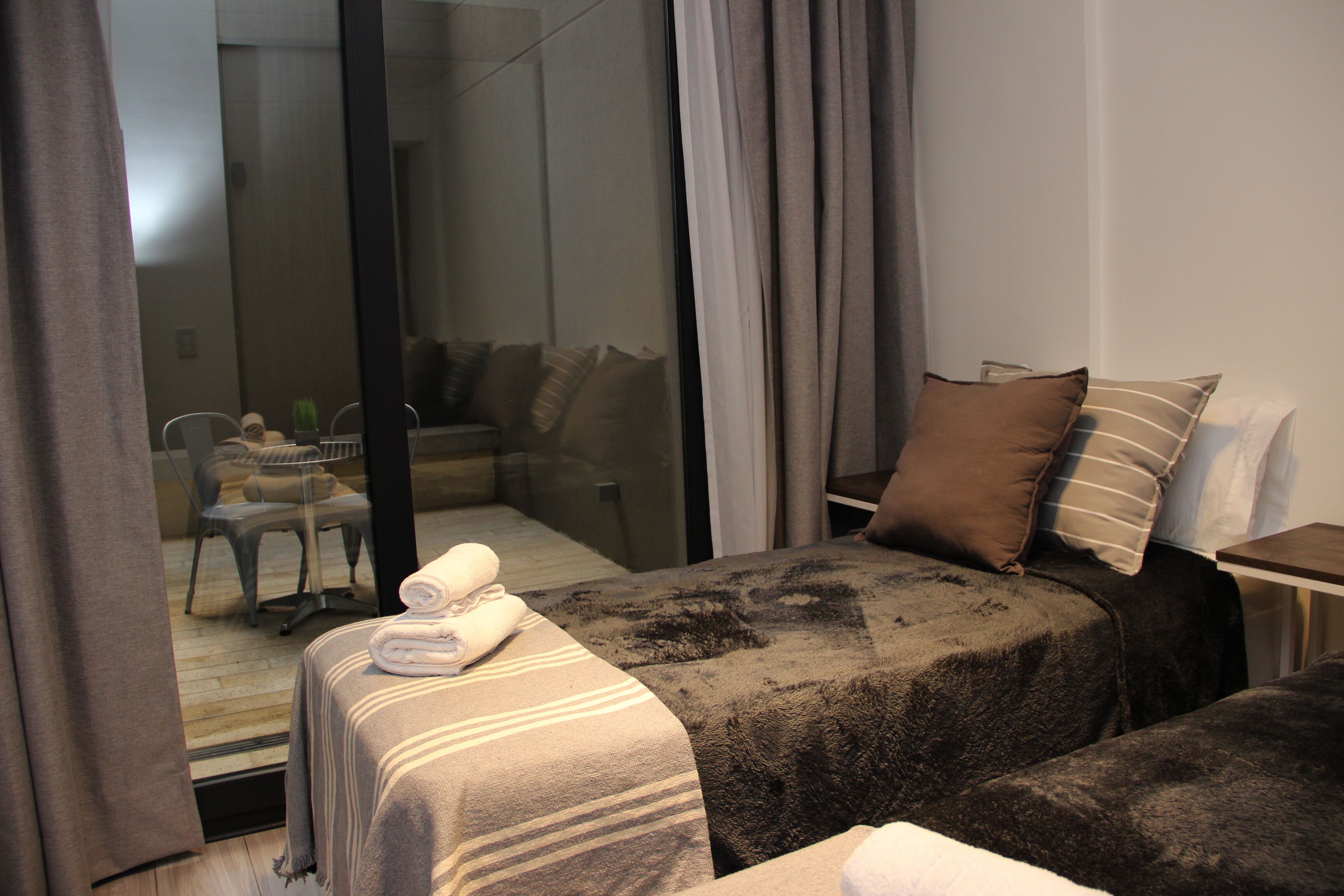 Quarto de hotel com duas camas, porta de vidro que dá para uma varanda e uma pequena mesa com uma cadeira.