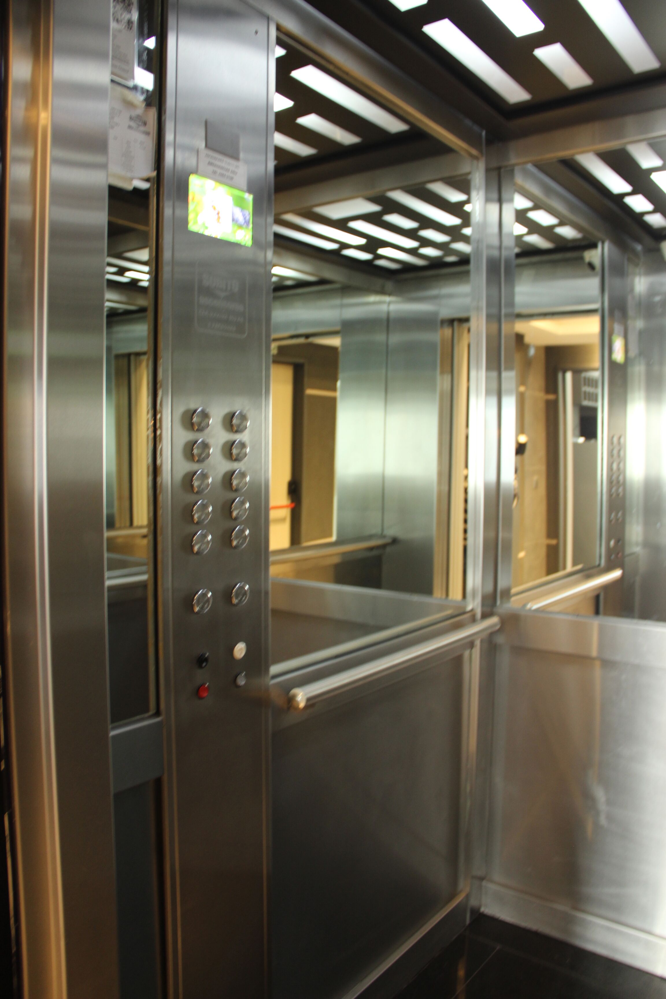 A metallic elevator interior with control buttons and a handrail.