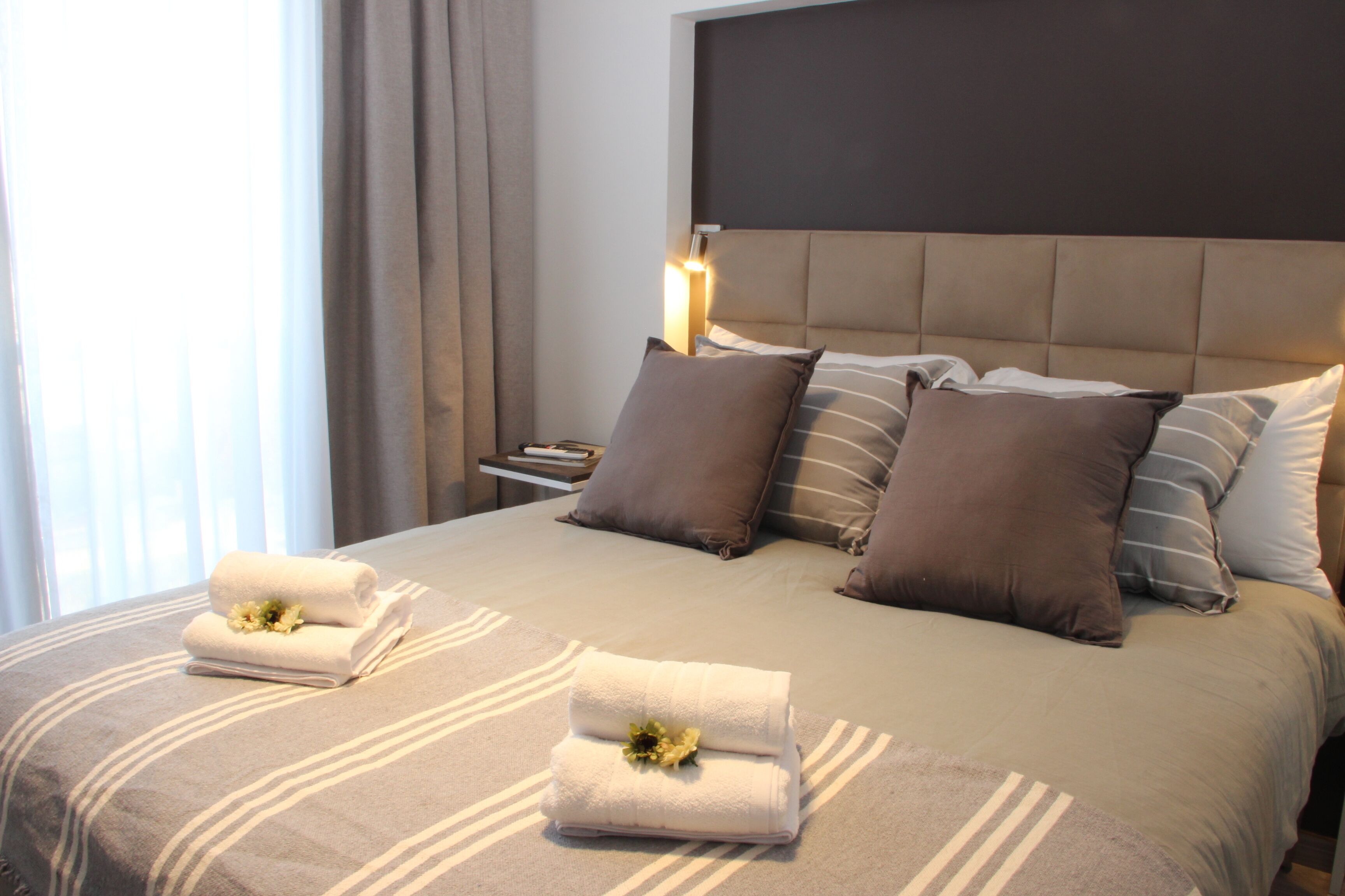 A neatly made bed with striped bedding, multiple pillows, and two folded towels with flowers.