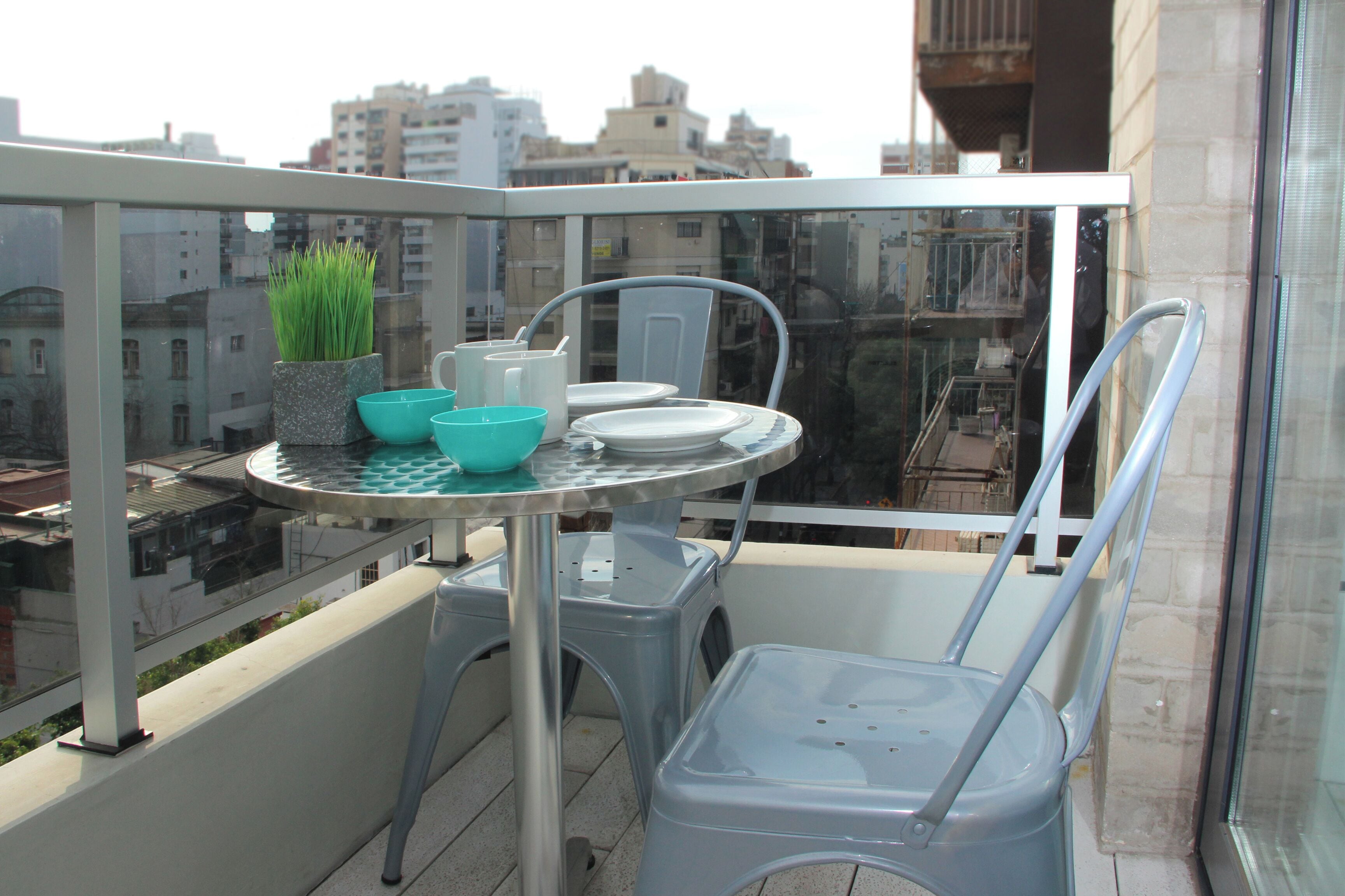 A balcony with a table, chairs, and a potted plant.