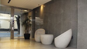 A modern lobby with a glass door entrance, a potted plant, and three white, uniquely shaped seating areas. - In House BA - Le Coq (Buenos Aires)