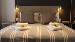 A neatly made bed with a striped bedspread, two pillows, and two folded towels with flowers. - In House BA - Le Coq (Buenos Aires)