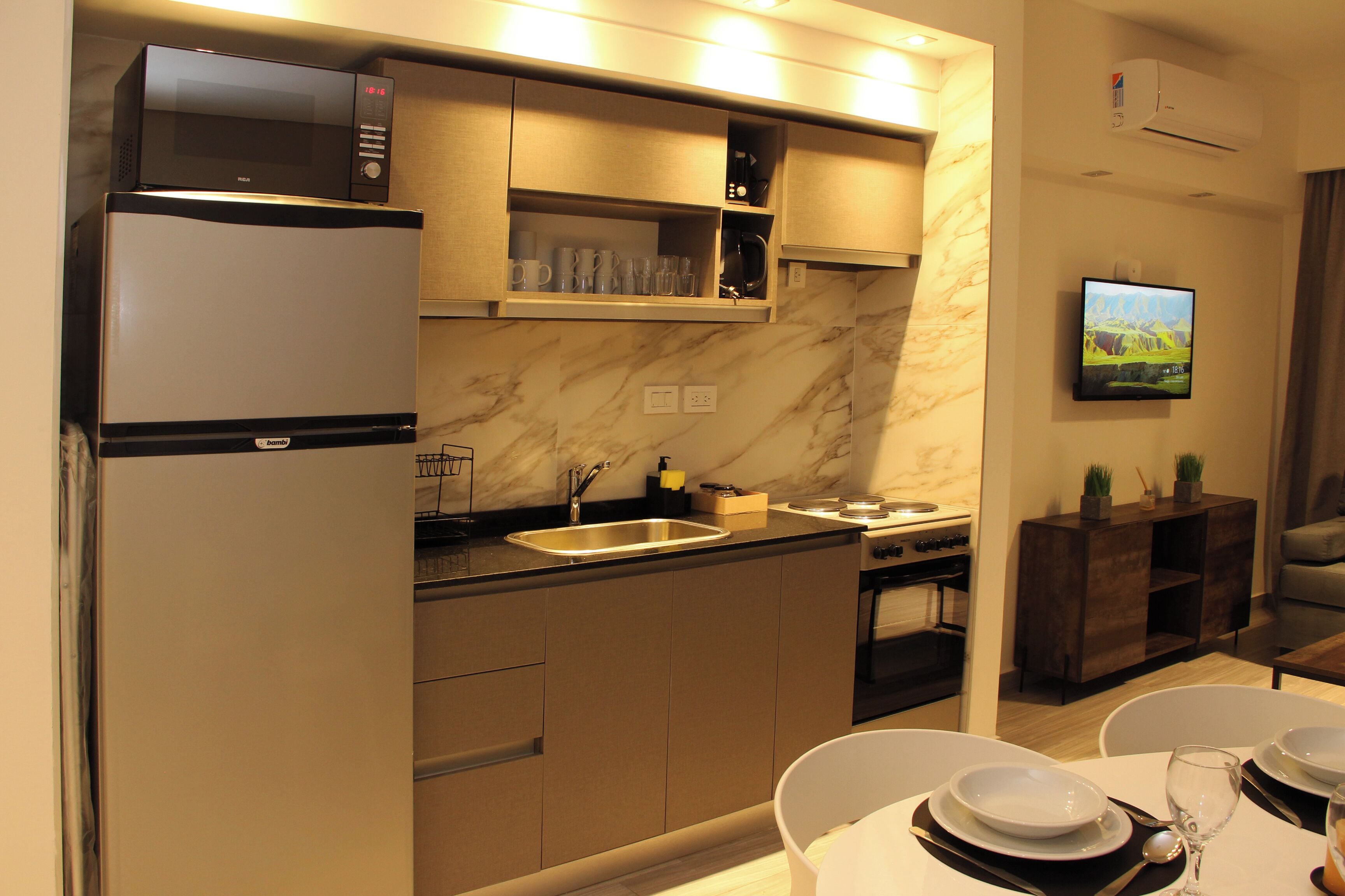 A modern kitchen with a built-in microwave, oven, and sink. There is a dining area with a table set for two, and a flat-screen TV mounted on the wall.