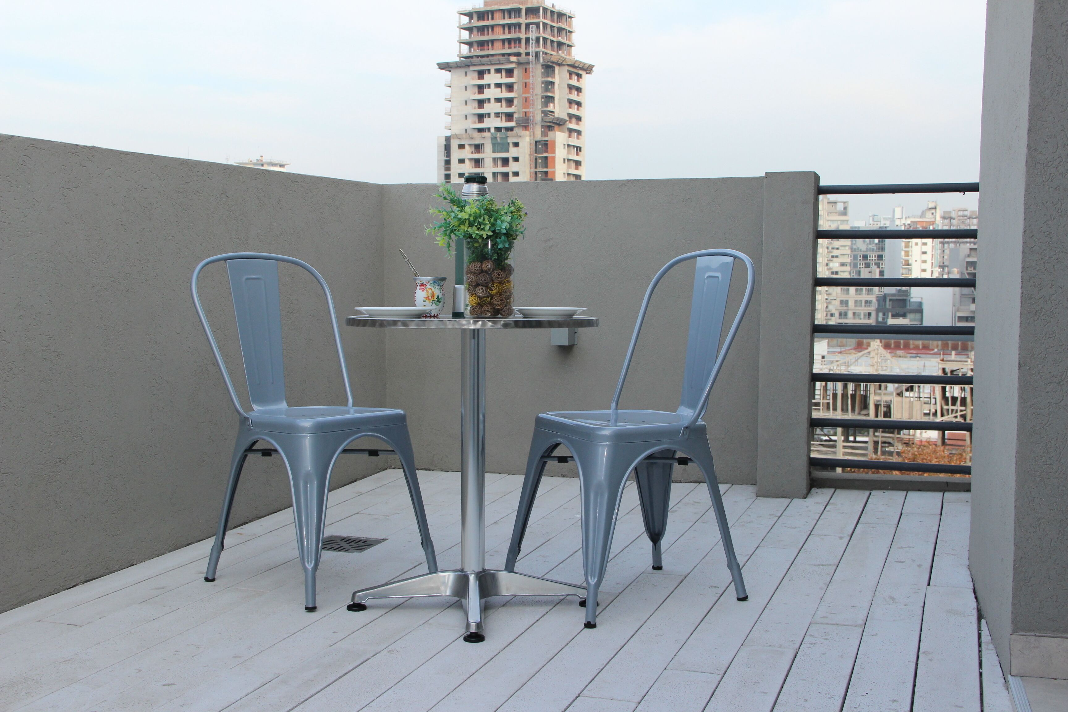 A balcony with two chairs and a table, a potted plant, and a view of a tall building in the background.