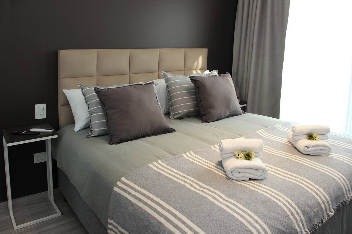 Una cama bien hecha con ropa de cama a rayas, un cabecero y dos toallas con motivos florales.
