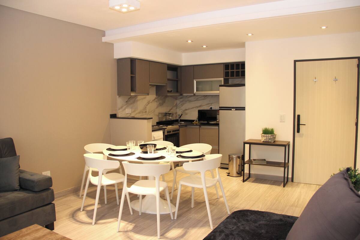 Una sala moderna con comedor, un sofá y una cocina al fondo.