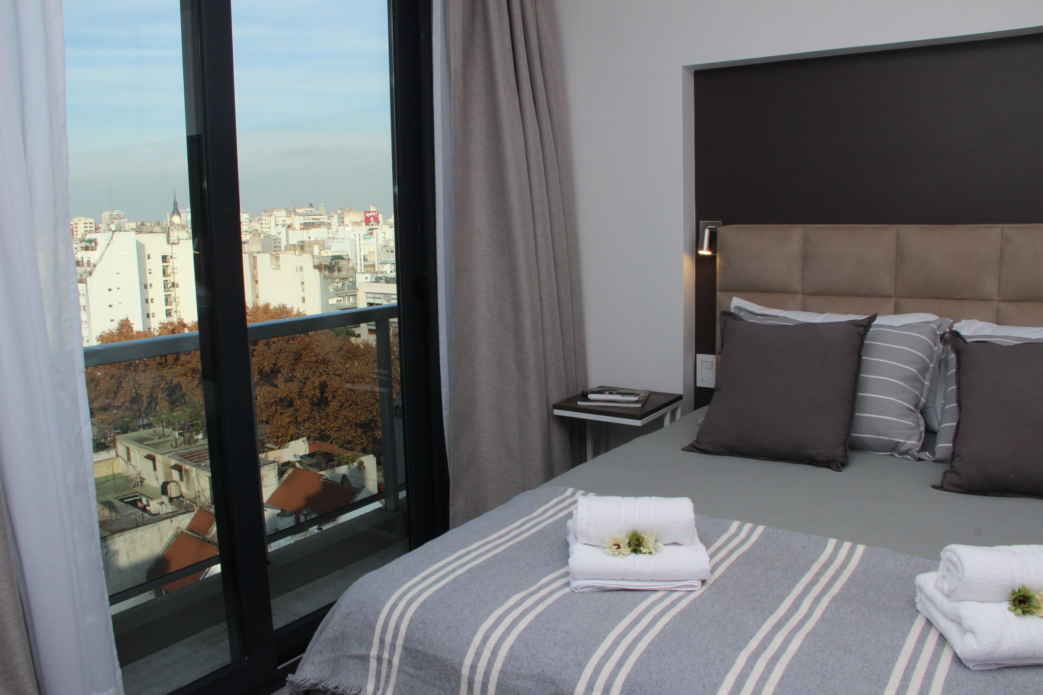 A modern hotel room with a large bed, a view of the city, and a small bedside table.