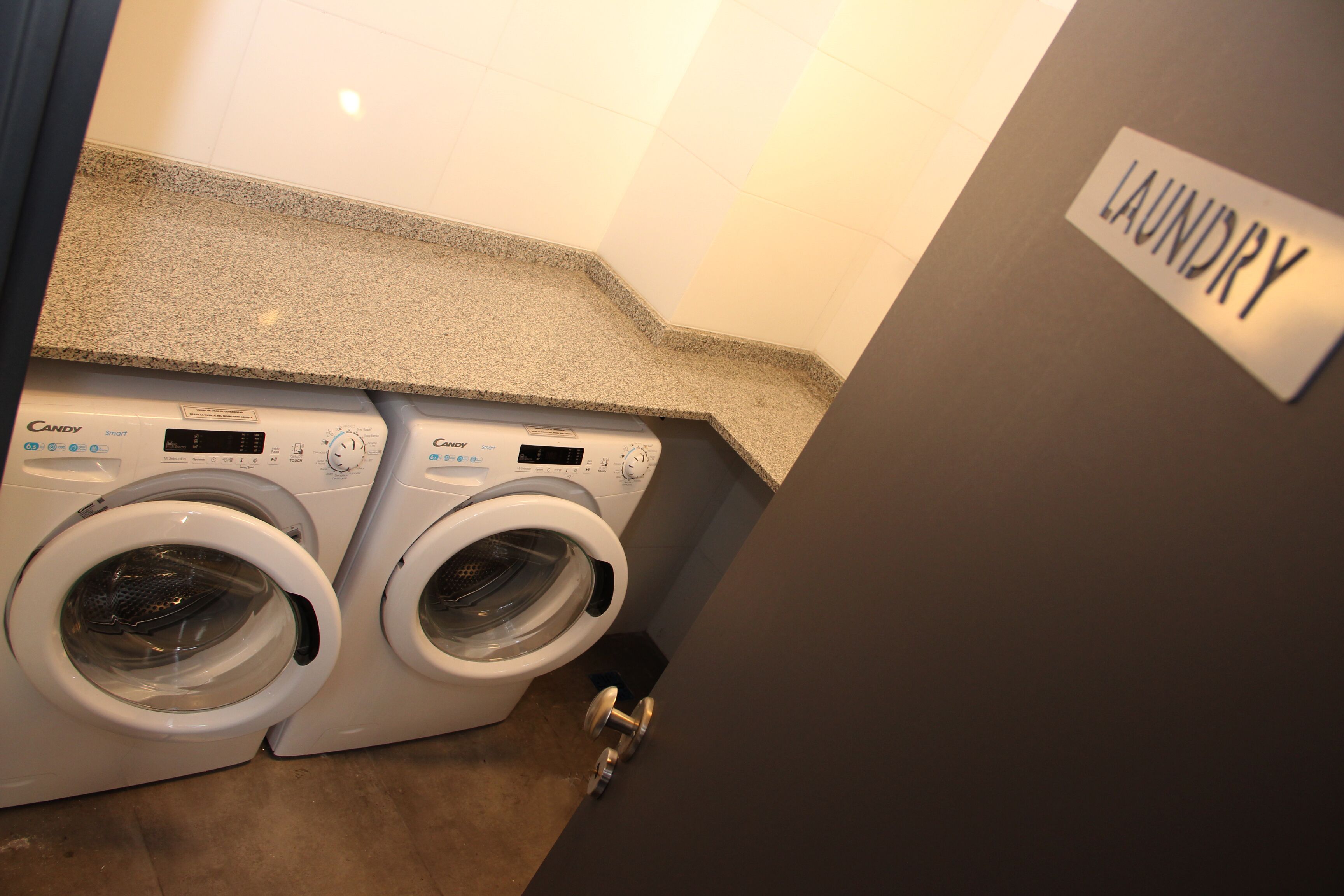 A laundry area with two Candy brand front-loading washing machines and a sign that reads "LAUNDRY".