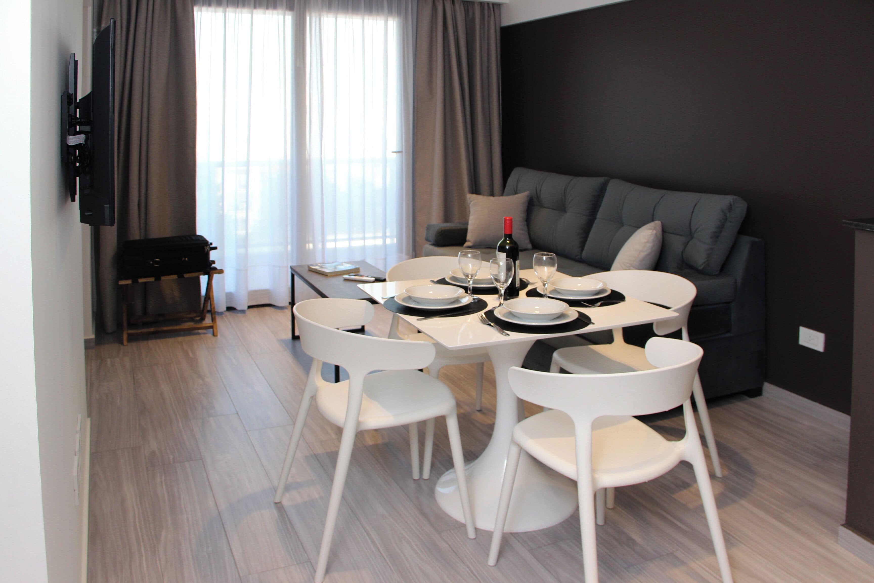 Een moderne woonkamer met een eethoek, met een bank, een flatscreen televisie, een eettafel met stoelen en een fles wijn.