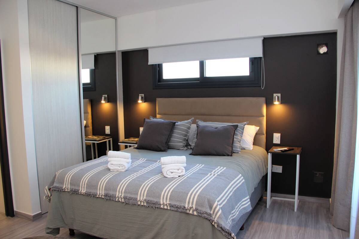 Una habitación de hotel moderna con una cama grande, mesitas de noche y un espejo.