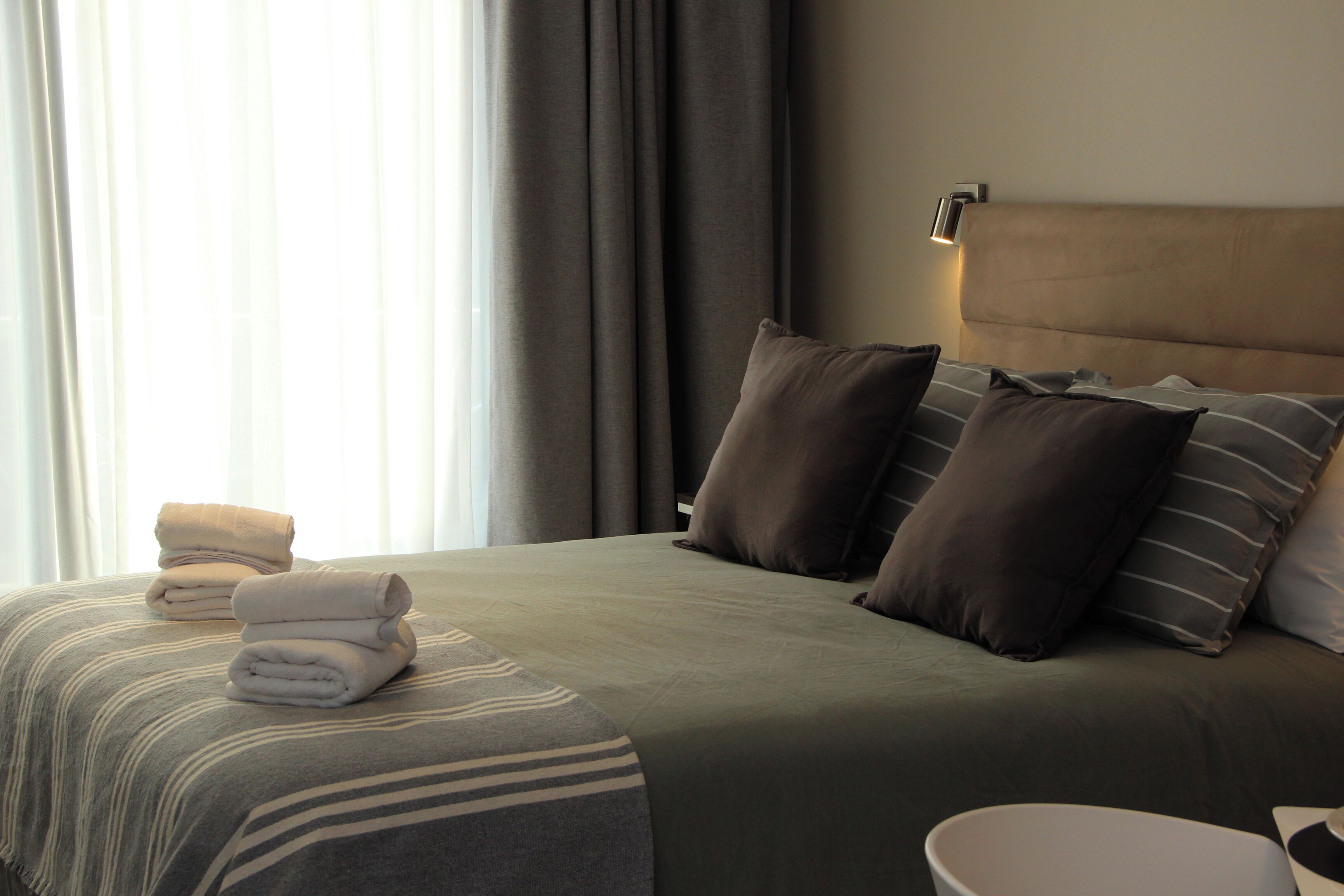 A neatly made bed with a striped bedspread, several pillows, and folded towels on the side.