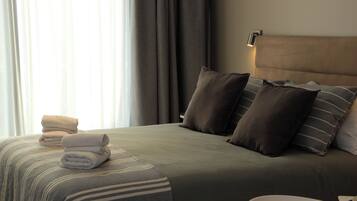 A neatly made bed with a striped bedspread, several pillows, and folded towels on the side.