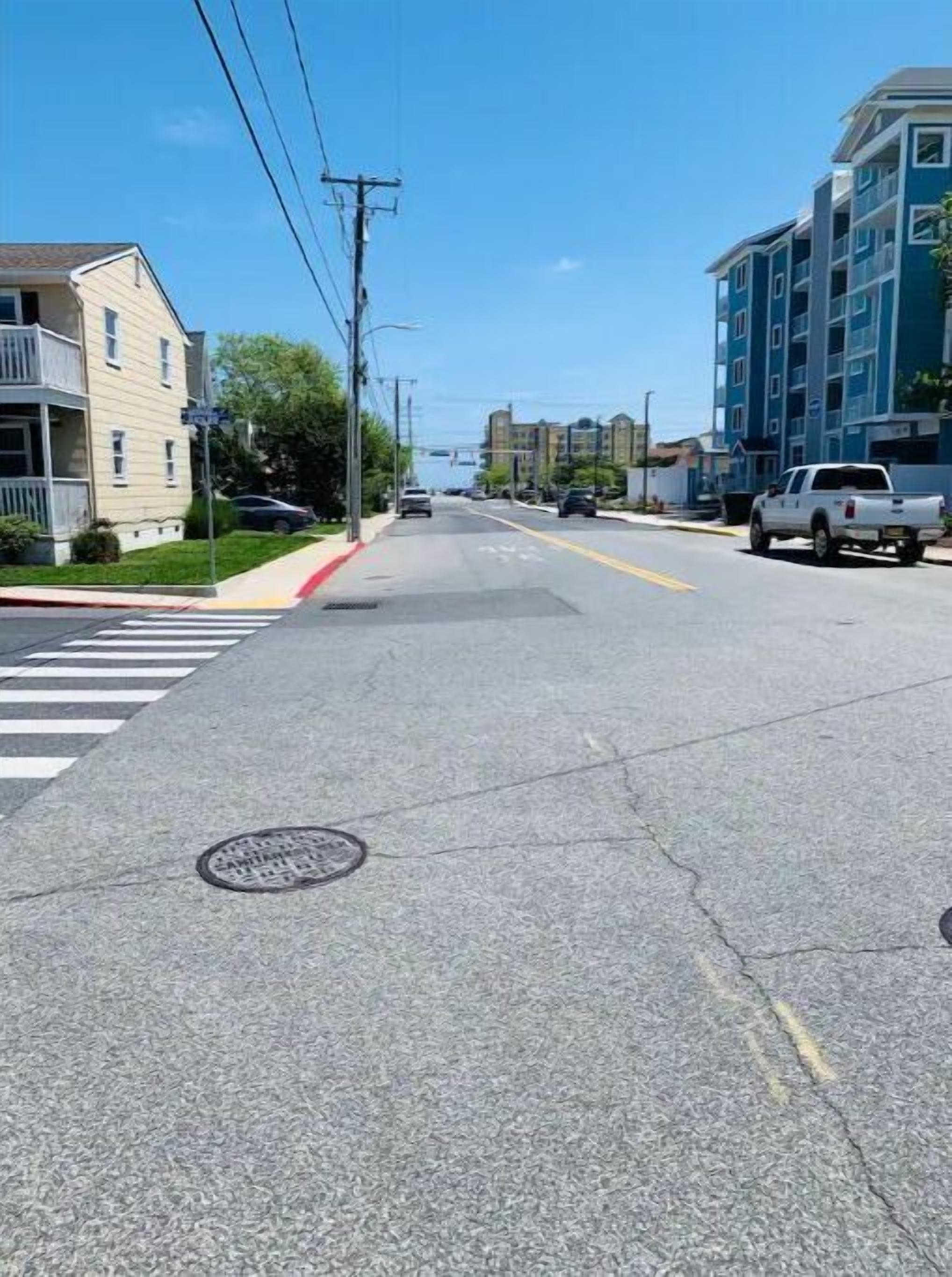 Une rue bordée de bâtiments des deux côtés, un passage piéton et un couvercle d’accès à une bouche d’égout.
