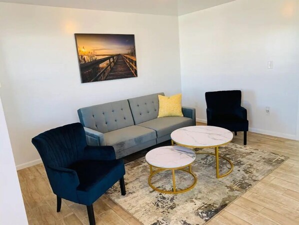 A living room with a grey sofa, a blue armchair, a black armchair, and a marble coffee table.