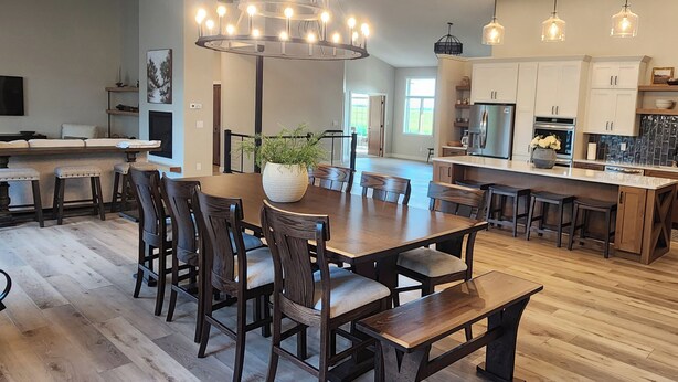 A spacious kitchen with a large island, wooden dining table, and chairs. There is a chandelier above the dining area and pendant lights above the kitchen island. - Beautiful, remodeled home on Lake Andrew with optional Pontoon Rental! (New London)