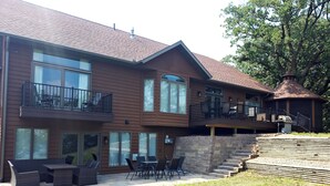 A two-story house with a patio, outdoor furniture, and a stone staircase leading to a deck. - Beautiful, remodeled home on Lake Andrew with optional Pontoon Rental! (New London)