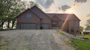 A two-story house with a gravel driveway, a brick garage, and a small porch area. - Beautiful, remodeled home on Lake Andrew with optional Pontoon Rental! (New London)