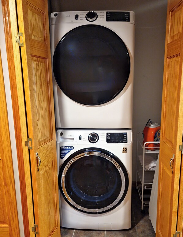 A stacked washer and dryer unit in a laundry room with wooden doors.
