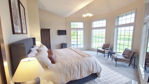 A bedroom with a large bed, a bedside table with a lamp, a chair, and a TV on the wall. - Beautiful, remodeled home on Lake Andrew with optional Pontoon Rental! (New London)