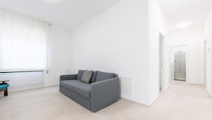 Un salón moderno y minimalista con un sofá gris, una mesita y una ventana con cortinas blancas.