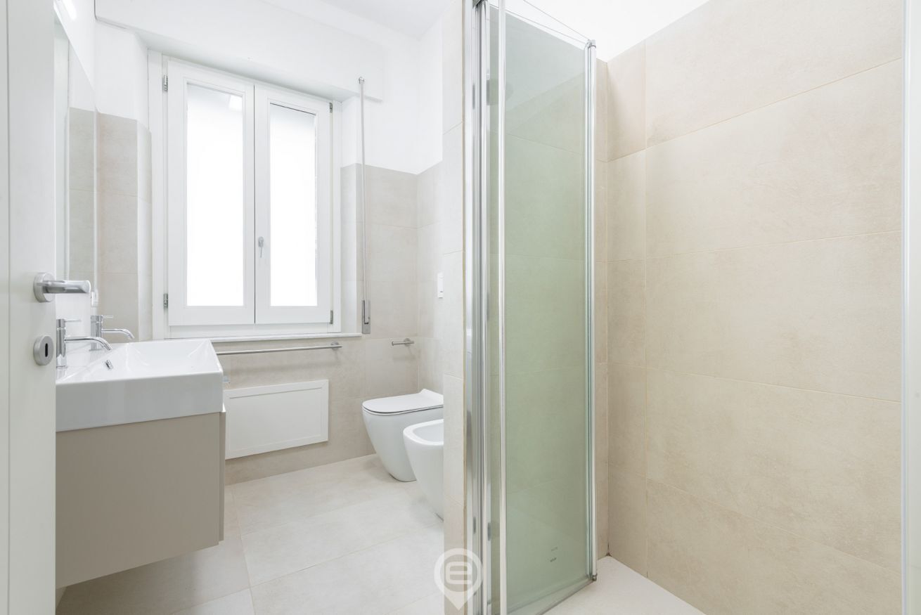 A modern bathroom with a glass shower enclosure, a white sink, and a toilet.