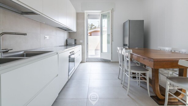 Una cocina moderna con armarios blancos, un lavamanos de acero inoxidable y una mesa de comedor de madera con sillas blancas.