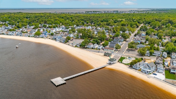 Vue aérienne d’une ville côtière avec une plage de sable, une jetée et des maisons d’habitation.